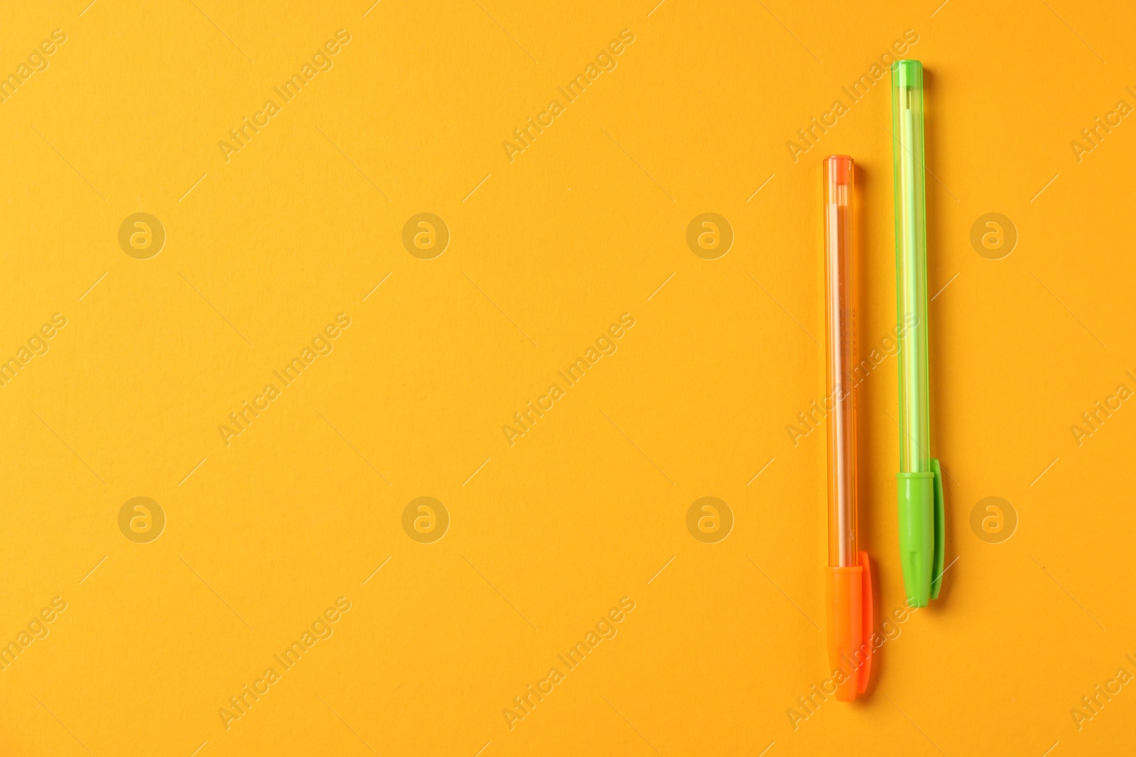 Stylish pens on orange background, top view. Space for text Photo of Stylish pens on orange background, top view. Space for text