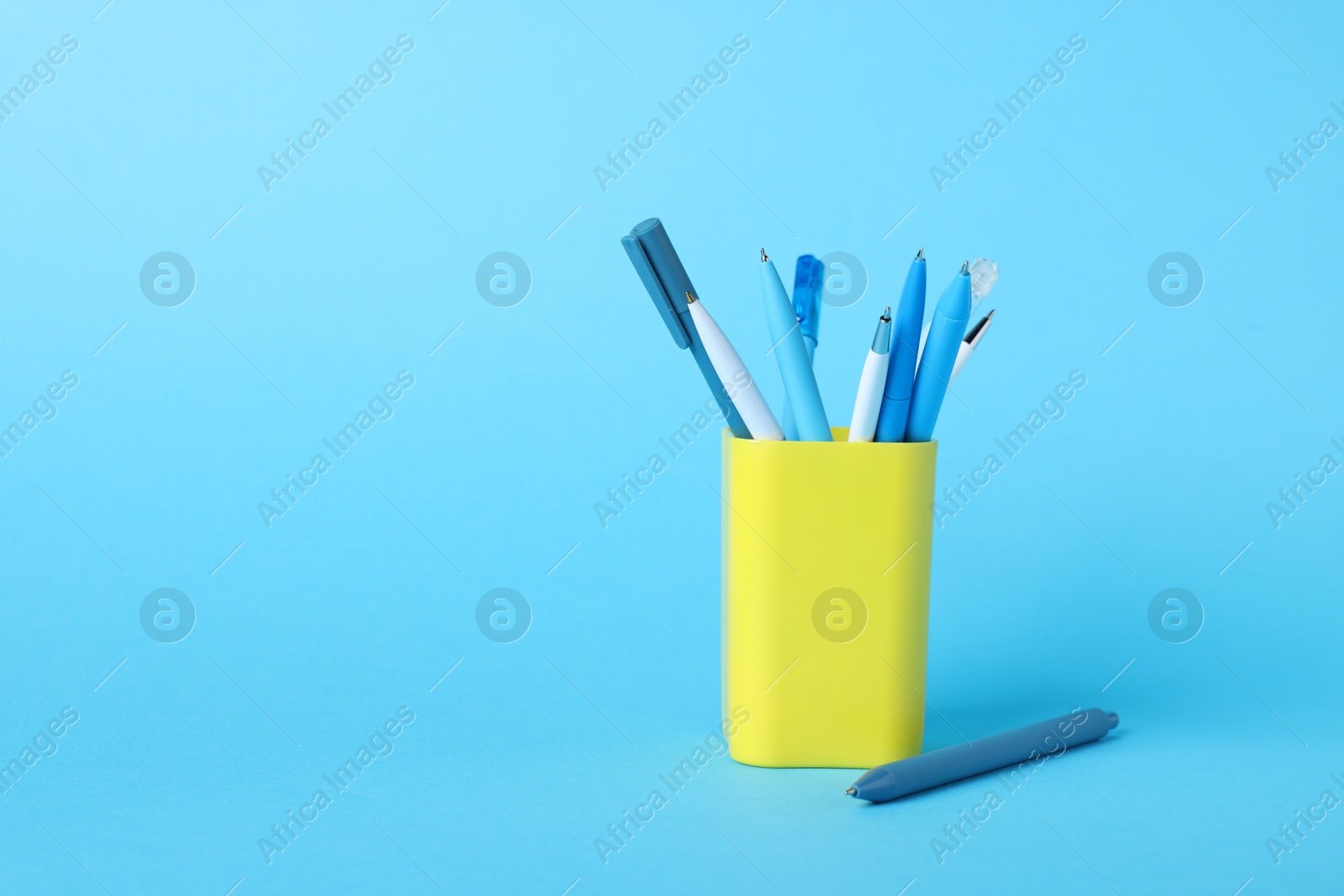 Ballpoint pens in holder on light blue background. Space for text Photo of Ballpoint pens in holder on light blue background. Space for text