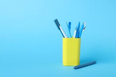 Photo of Ballpoint pens in holder on light blue background. Space for text