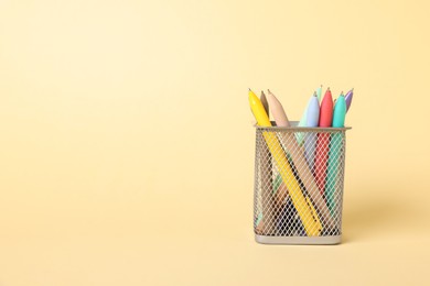 Photo of Ballpoint pens in holder on beige background, closeup. Space for text