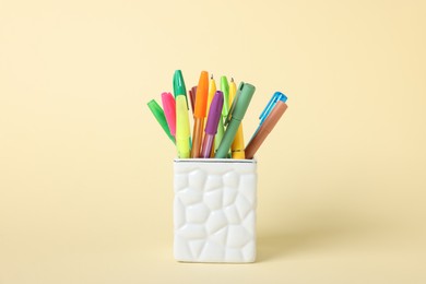 Photo of Ballpoint pens in holder on beige background, closeup