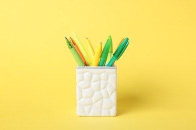 Photo of Ballpoint pens in holder on yellow background, closeup