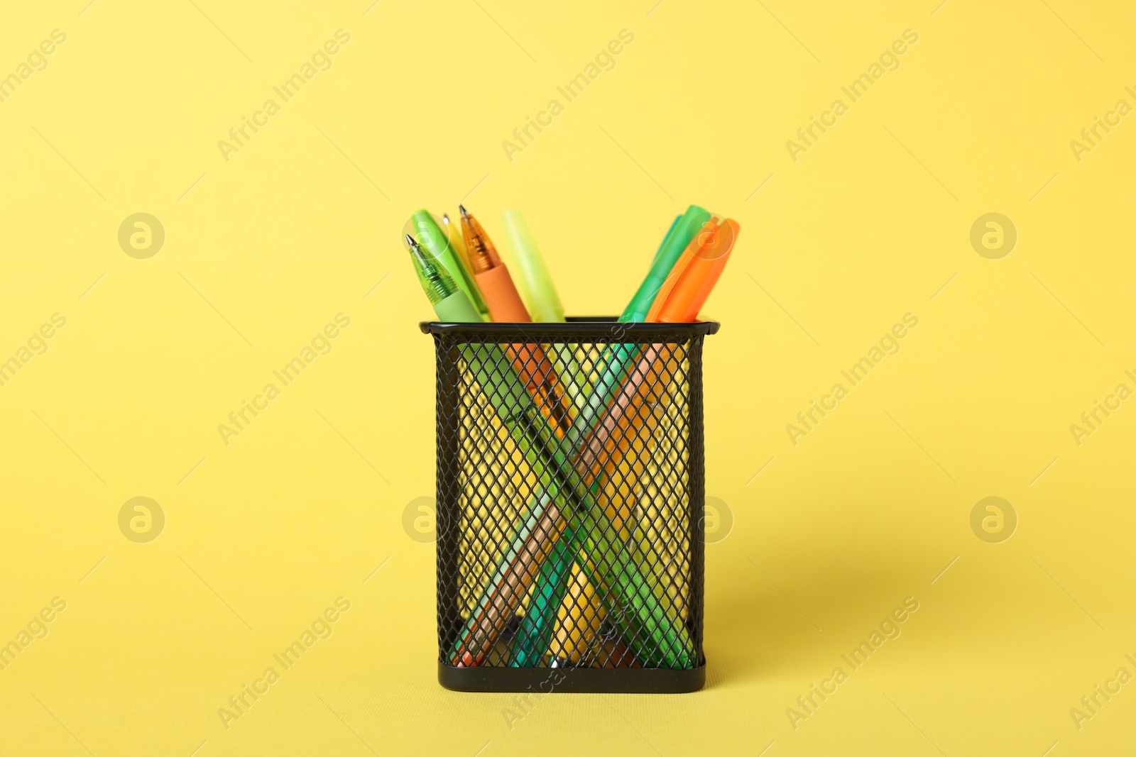 Ballpoint pens in holder on yellow background, closeup Photo of Ballpoint pens in holder on yellow background, closeup