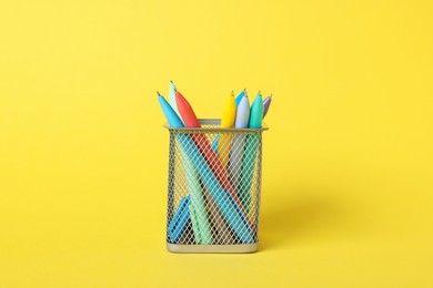 Photo of Ballpoint pens in holder on yellow background, closeup