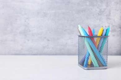 Photo of Ballpoint pens in holder on light wooden table against grey background. Space for text