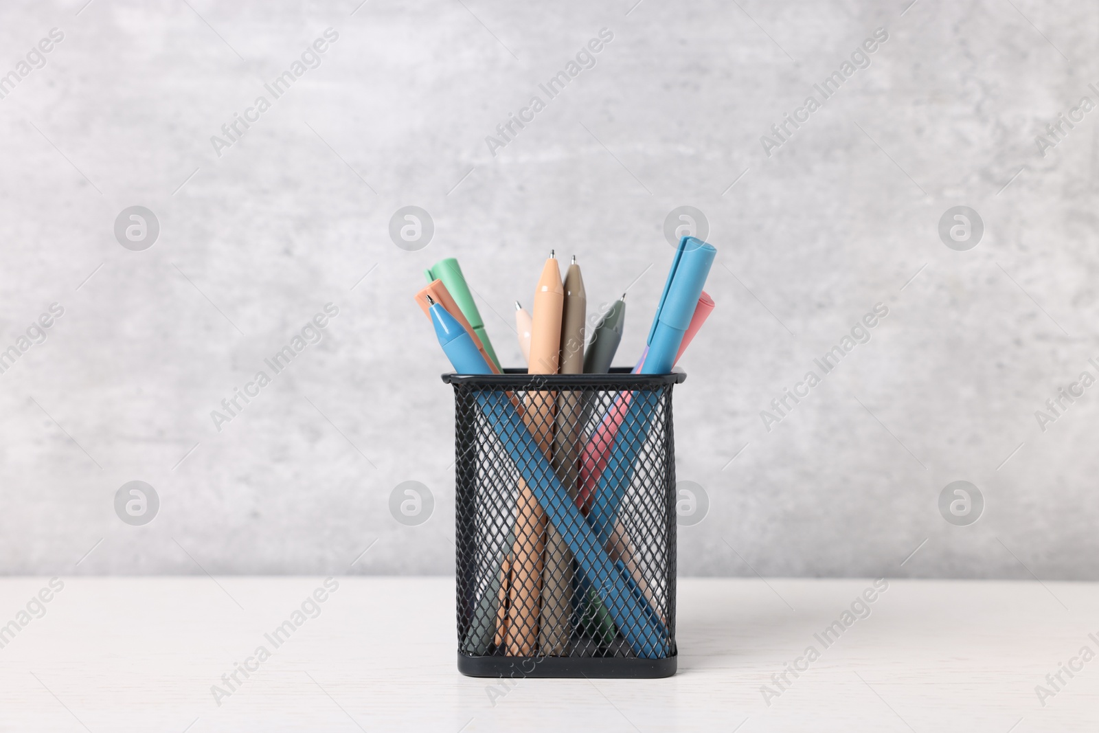 Ballpoint pens in holder on light wooden table against grey background Photo of Ballpoint pens in holder on light wooden table against grey background
