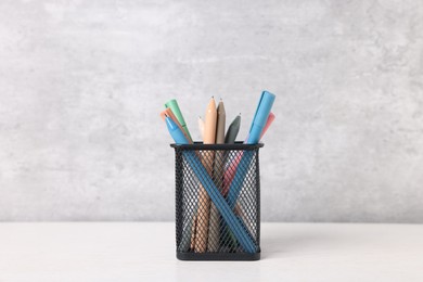 Photo of Ballpoint pens in holder on light wooden table against grey background