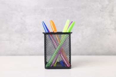 Photo of Ballpoint pens in holder on light wooden table against grey background, closeup