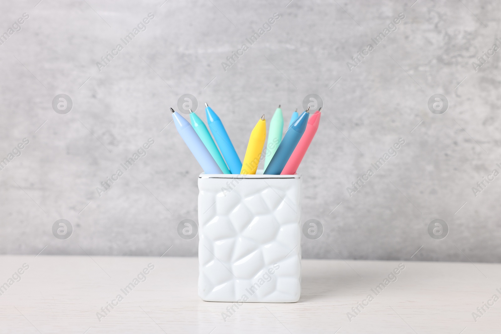 Ballpoint pens in holder on light wooden table against grey background, closeup Photo of Ballpoint pens in holder on light wooden table against grey background, closeup