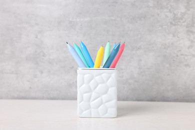 Photo of Ballpoint pens in holder on light wooden table against grey background, closeup