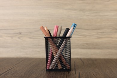 Photo of Ballpoint pens in holder on wooden table, closeup