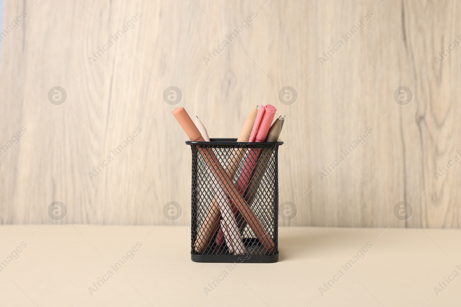 Ballpoint pens in holder on beige table against wooden background Photo of Ballpoint pens in holder on beige table against wooden background