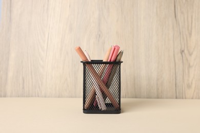 Photo of Ballpoint pens in holder on beige table against wooden background