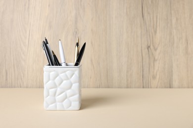 Photo of Ballpoint pens in holder on beige table against wooden background. Space for text