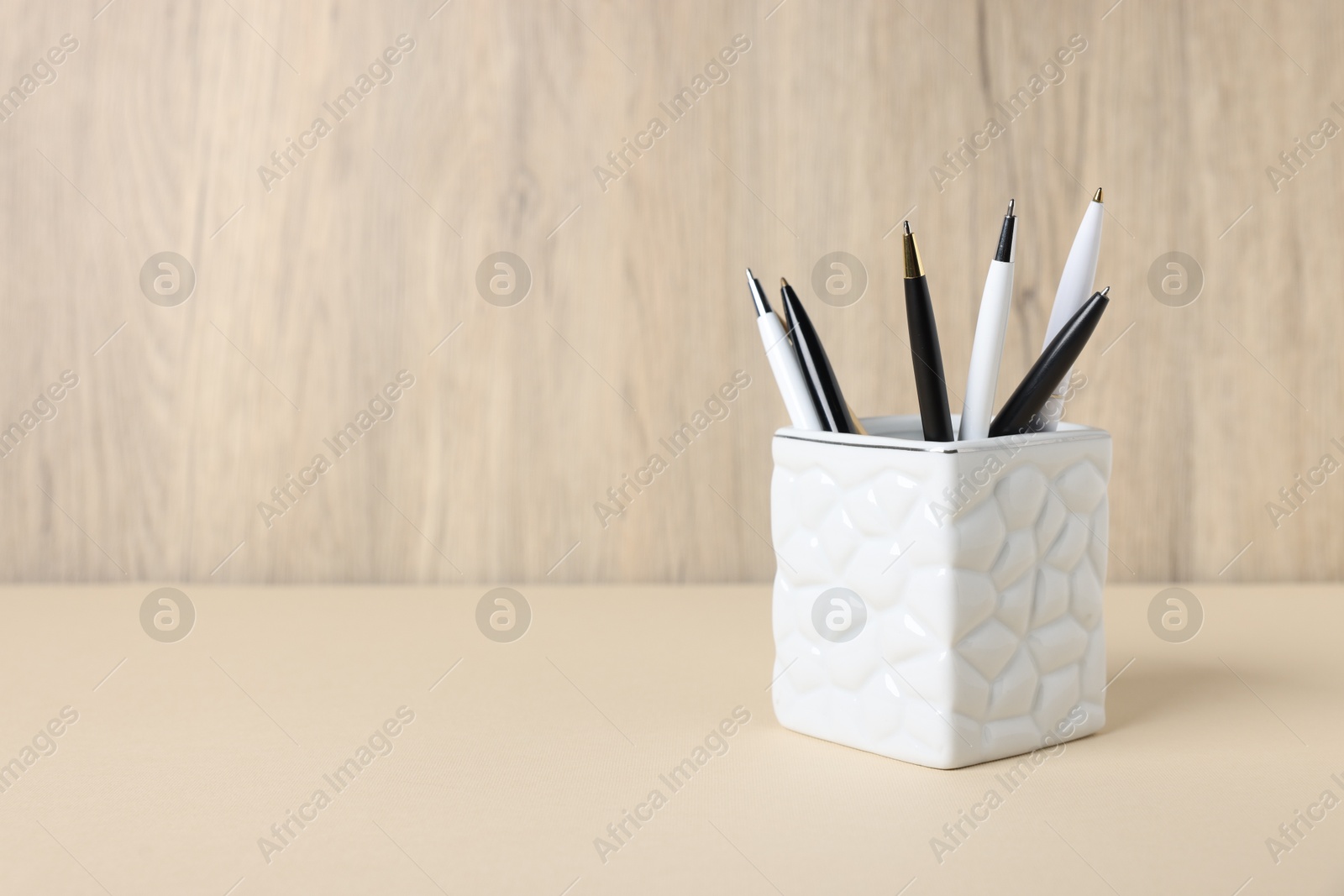 Ballpoint pens in holder on beige table against wooden background. Space for text Photo of Ballpoint pens in holder on beige table against wooden background. Space for text