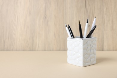 Photo of Ballpoint pens in holder on beige table against wooden background. Space for text