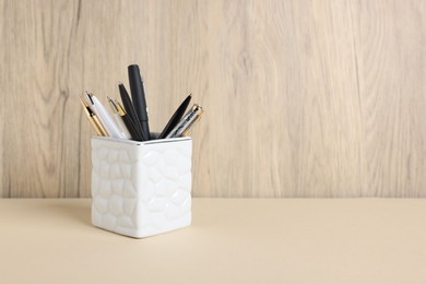 Photo of Ballpoint pens in holder on beige table against wooden background. Space for text