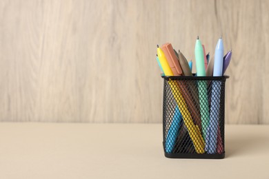 Photo of Ballpoint pens in holder on beige table against wooden background, closeup. Space for text