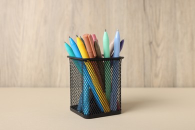 Photo of Ballpoint pens in holder on beige table against wooden background, closeup