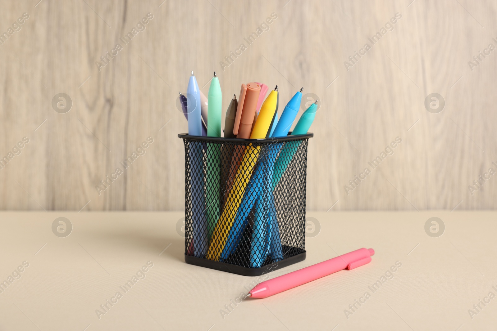 Ballpoint pens in holder on beige table against wooden background Photo of Ballpoint pens in holder on beige table against wooden background