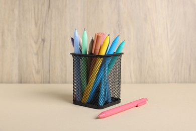 Photo of Ballpoint pens in holder on beige table against wooden background