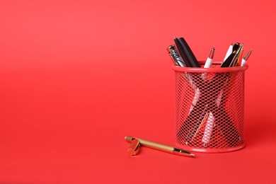 Photo of Ballpoint pens in holder on red background, closeup. Space for text