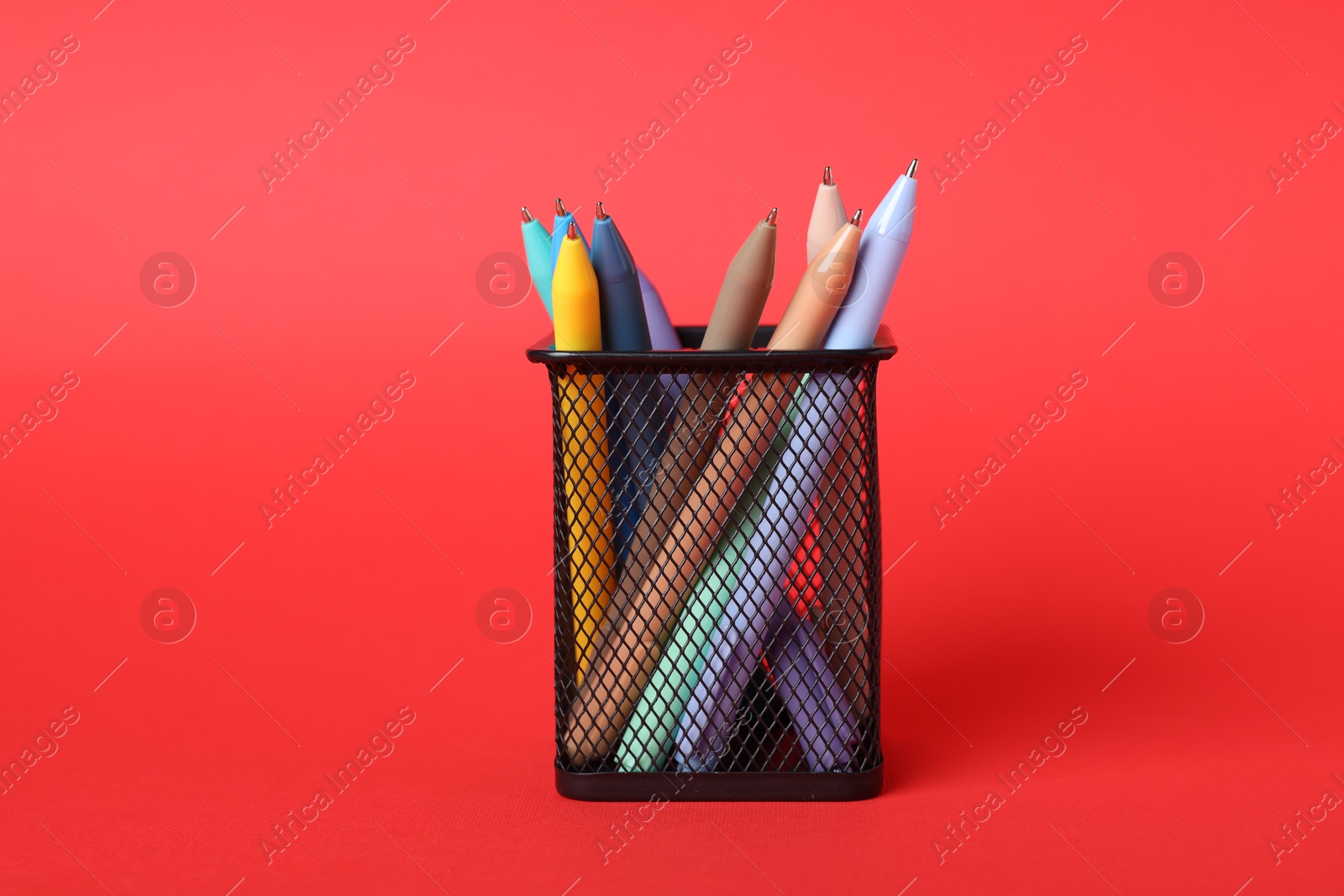 Ballpoint pens in holder on red background, closeup Photo of Ballpoint pens in holder on red background, closeup