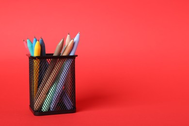 Photo of Ballpoint pens in holder on red background, closeup. Space for text