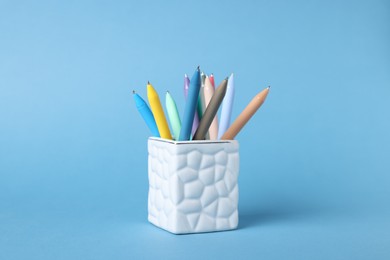 Photo of Ballpoint pens in holder on light blue background, closeup