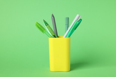 Photo of Ballpoint pens in holder on green background, closeup