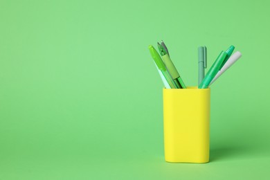 Photo of Ballpoint pens in holder on green background, closeup. Space for text