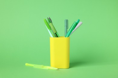 Photo of Ballpoint pens in holder on green background, closeup