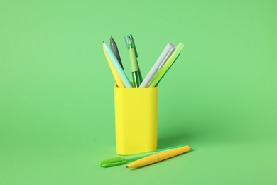 Photo of Ballpoint pens in holder on green background, closeup