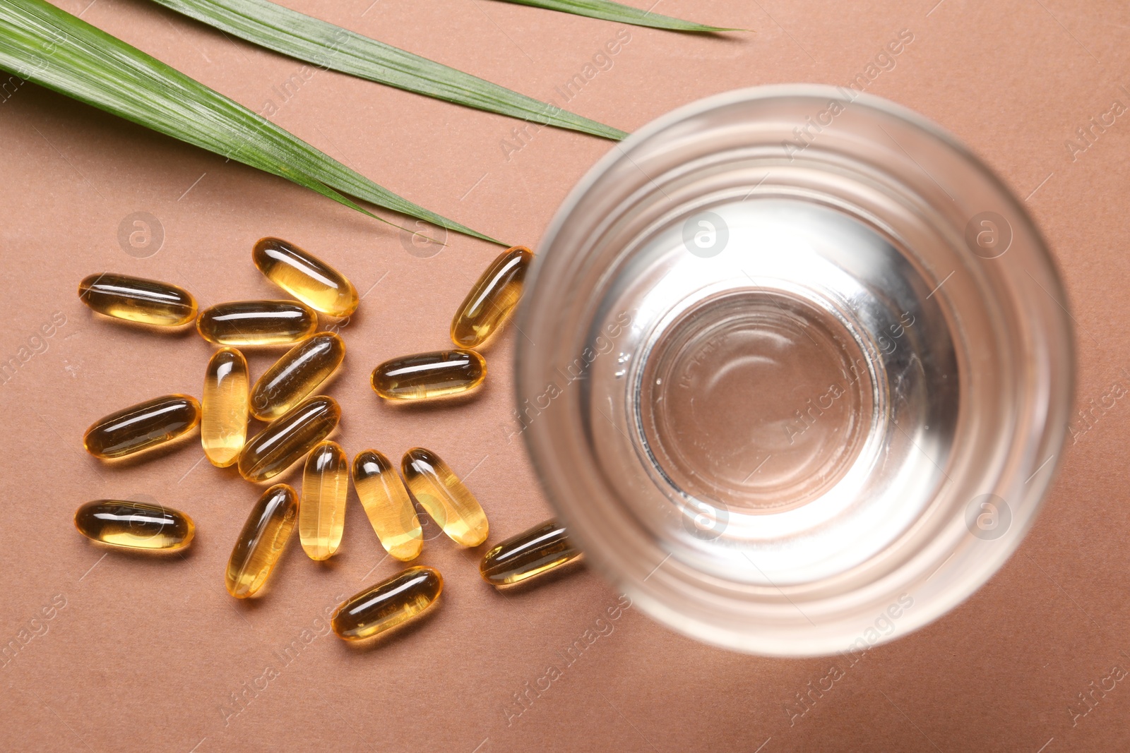 Collagen capsules, leaves and water on brown background, flat lay Photo of Collagen capsules, leaves and water on brown background, flat lay