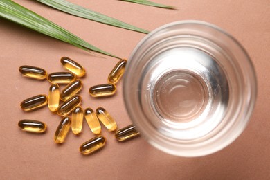Photo of Collagen capsules, leaves and water on brown background, flat lay
