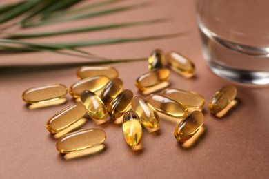 Photo of Collagen capsules, leaves and water on brown background, closeup