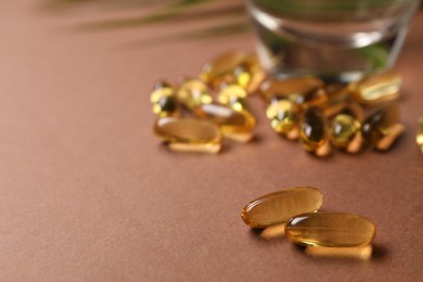 Photo of Collagen capsules and water on brown background, closeup. Space for text