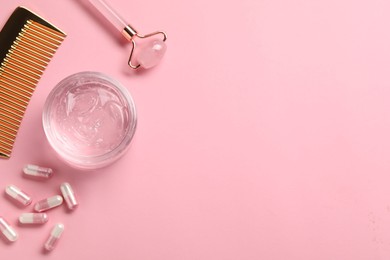 Photo of Collagen capsules, gel, comb and face roller on pink background, flat lay. Space for text