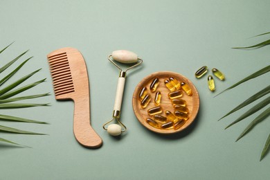 Photo of Collagen capsules, comb, face roller and leaves on light green background, flat lay