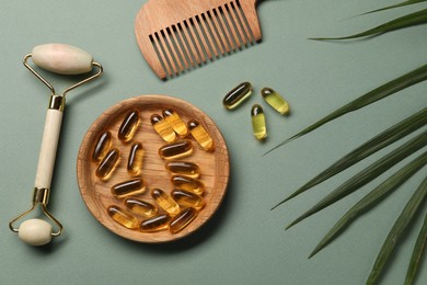 Photo of Collagen capsules, comb, face roller and leaves on light green background, flat lay