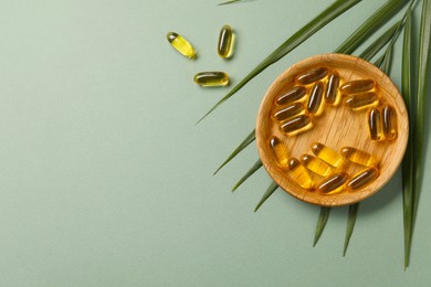 Photo of Collagen capsules and leaves on light green background, flat lay. Space for text