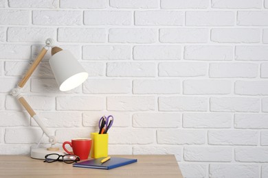 Photo of Different stationery, coffee, lamp and glasses on wooden office table near white brick wall, space for text