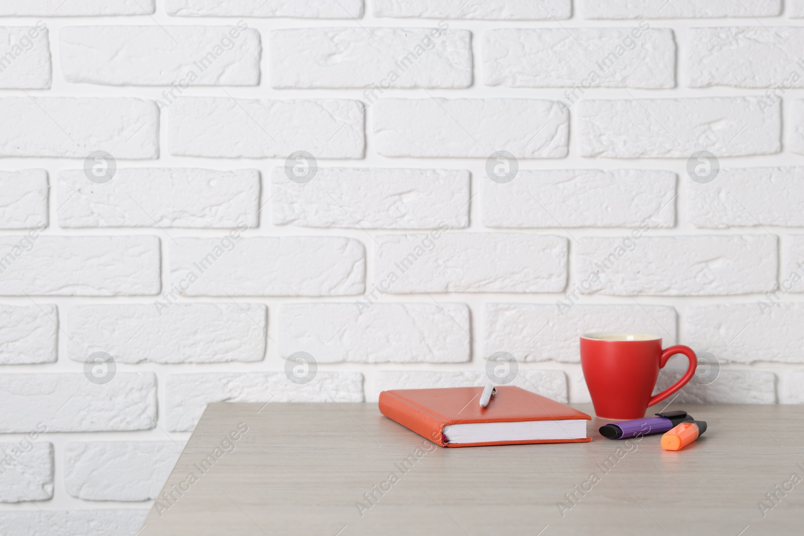 Different stationery and coffee on wooden office table near white brick wall Photo of Different stationery and coffee on wooden office table near white brick wall