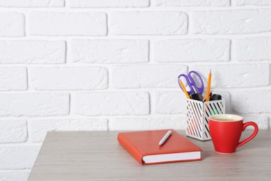 Photo of Different stationery and coffee on wooden office table near white brick wall