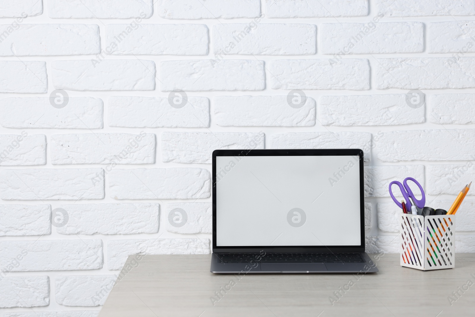Laptop and stationery on wooden office table near white brick wall, space for text Photo of Laptop and stationery on wooden office table near white brick wall, space for text