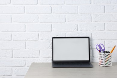 Photo of Laptop and stationery on wooden office table near white brick wall, space for text