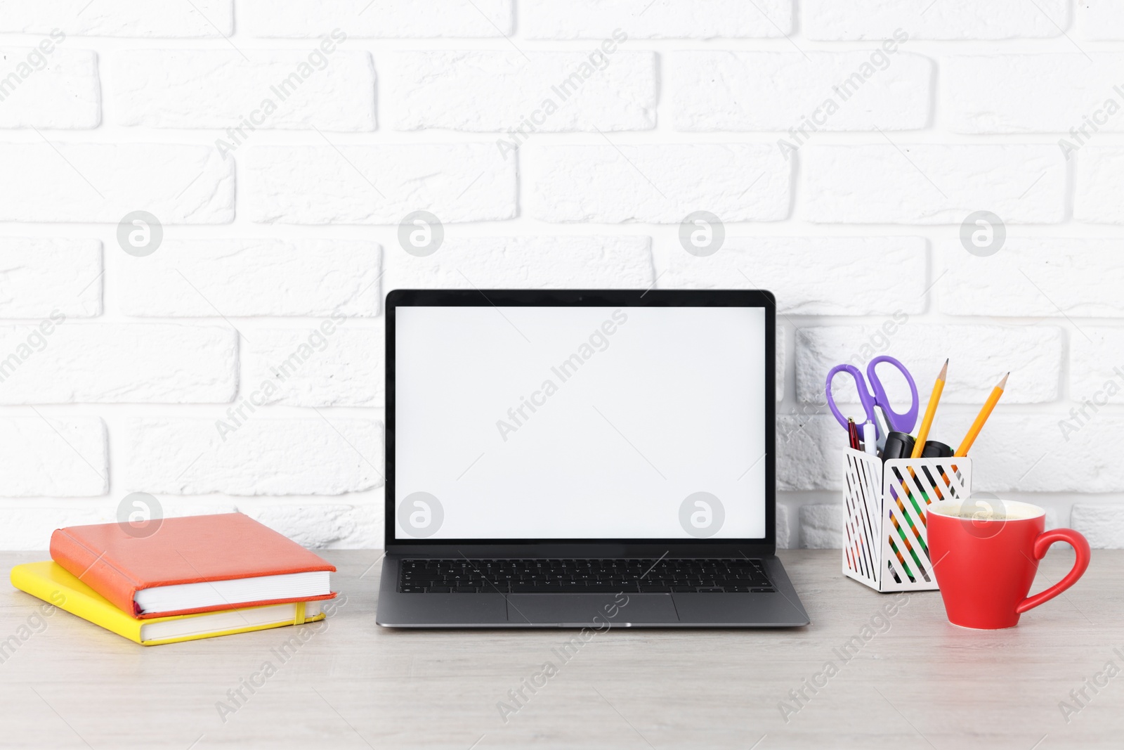 Laptop, stationery and coffee on wooden office table near white brick wall Photo of Laptop, stationery and coffee on wooden office table near white brick wall