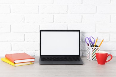 Photo of Laptop, stationery and coffee on wooden office table near white brick wall