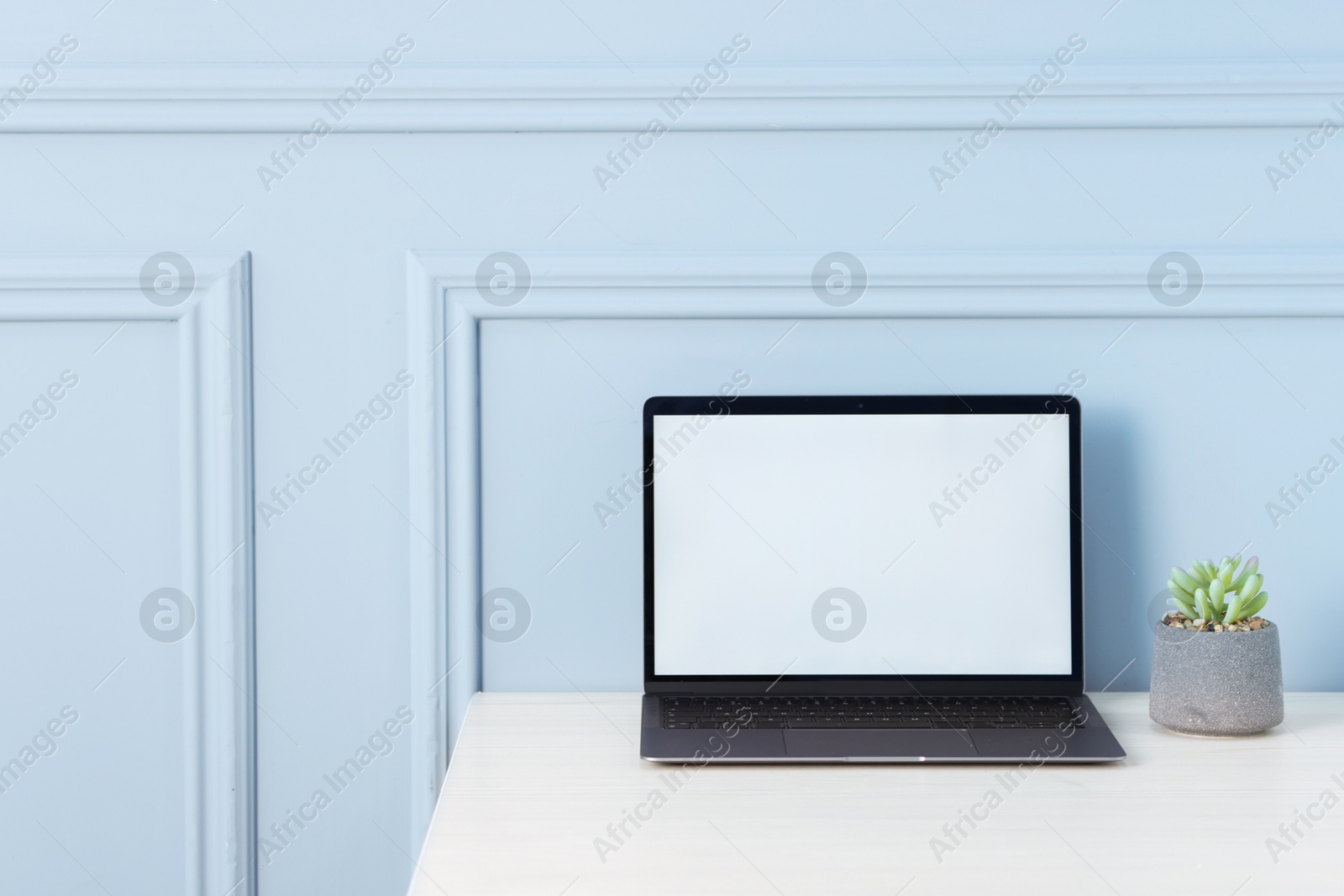 Laptop and floral decor on office table near light wall, space for text Photo of Laptop and floral decor on office table near light wall, space for text