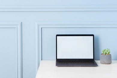 Photo of Laptop and floral decor on office table near light wall, space for text